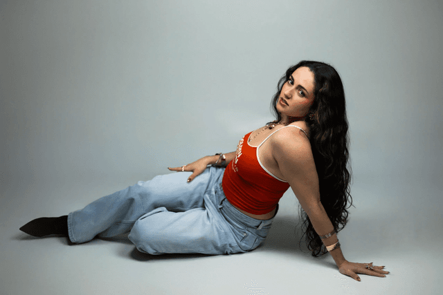 Caluu C. sentada en el suelo con camiseta roja y jeans anchos