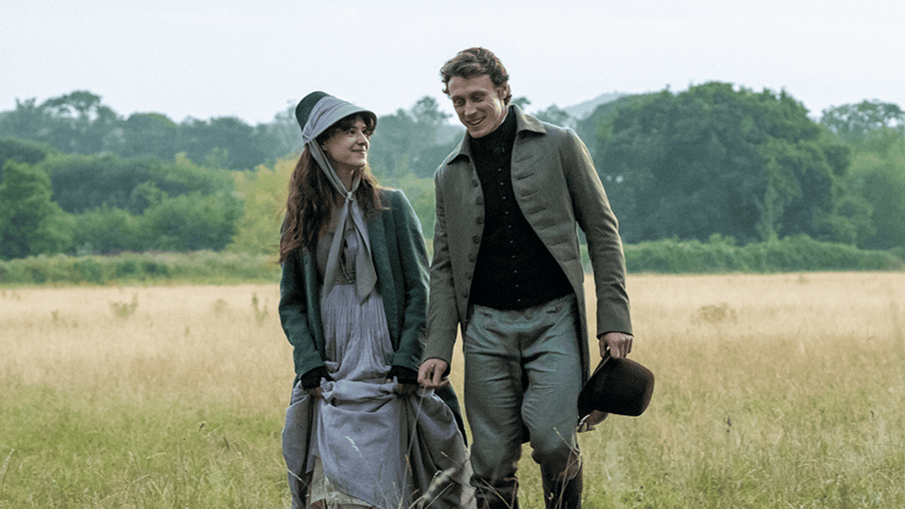 Una pareja con vestuario de época camina sonriente por un campo en una escena de «Sense and Sensibility»