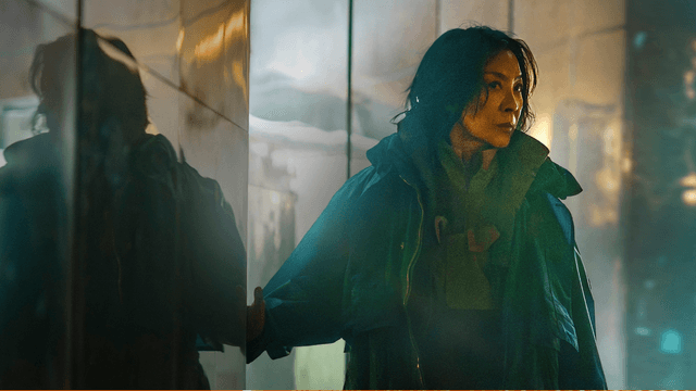 Michelle Yeoh como Olwen, con chaqueta verde oscura, junto a una pared de metal en una escena de «Blade Runner 2099»
