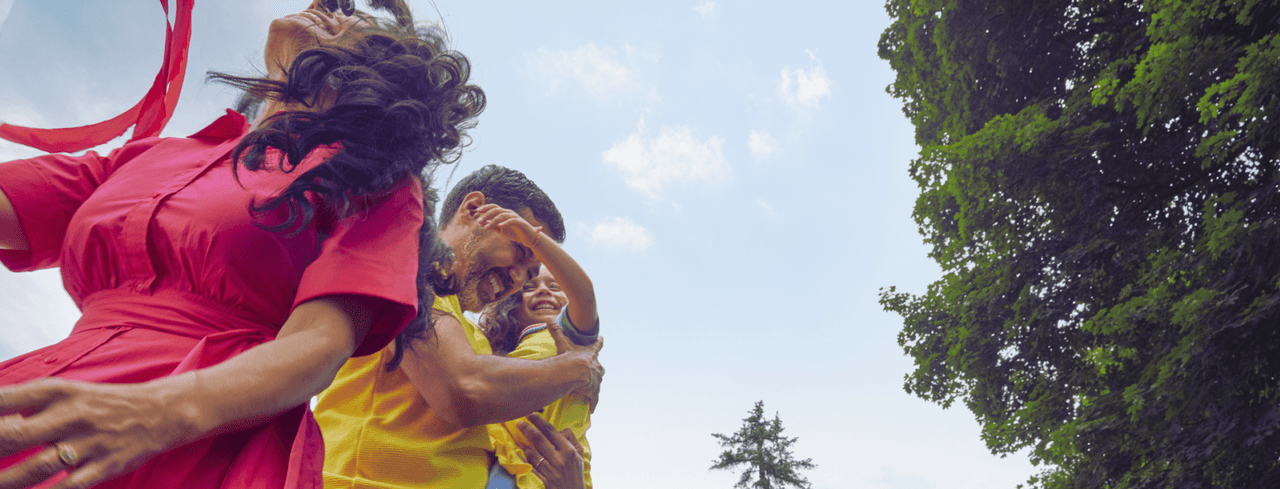 Una familia juega al aire libre: una mujer de vestido rojo y un hombre de amarillo cargan a un niño