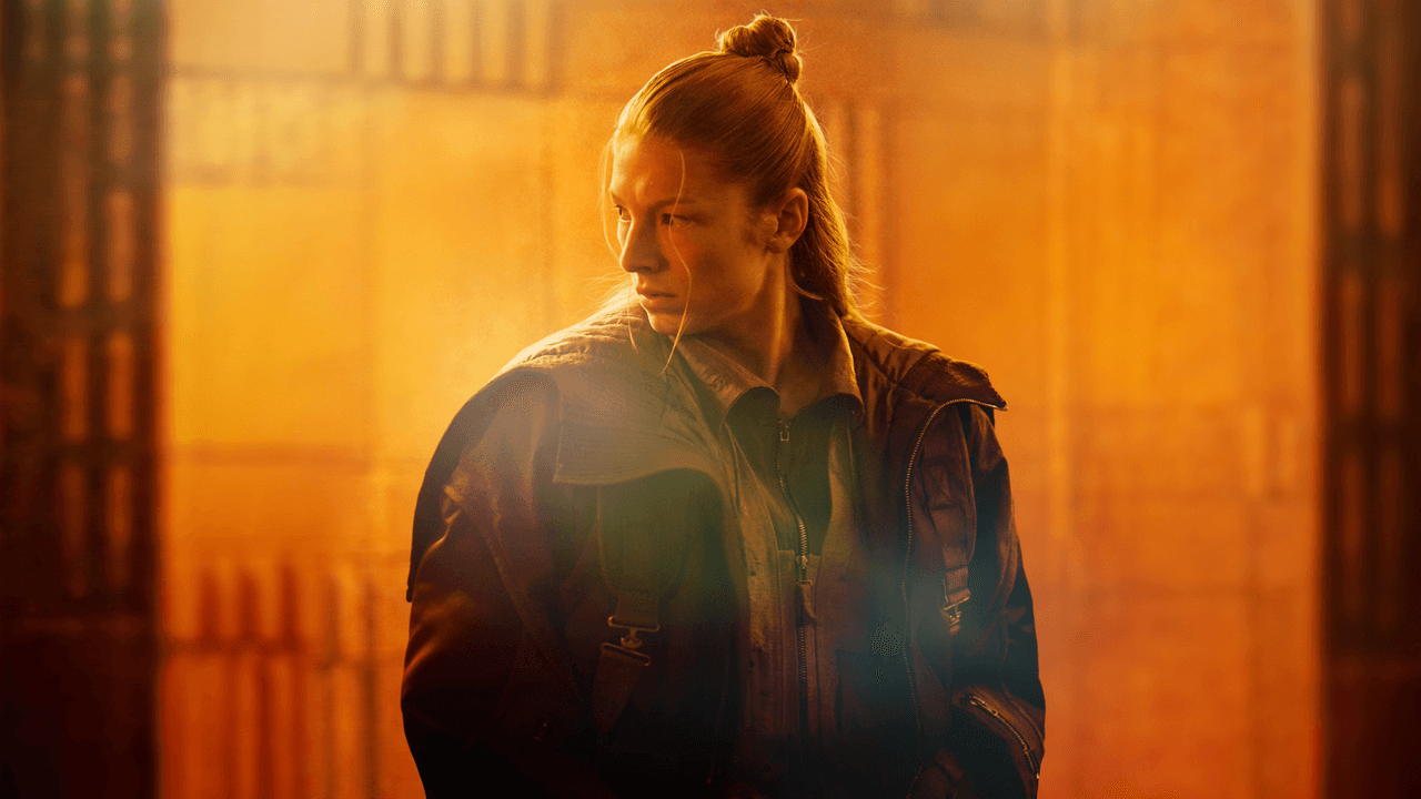 Hunter Schafer como Cora, con moño alto y chaqueta de cuero, frente a una luz naranja en «Blade Runner 2099»