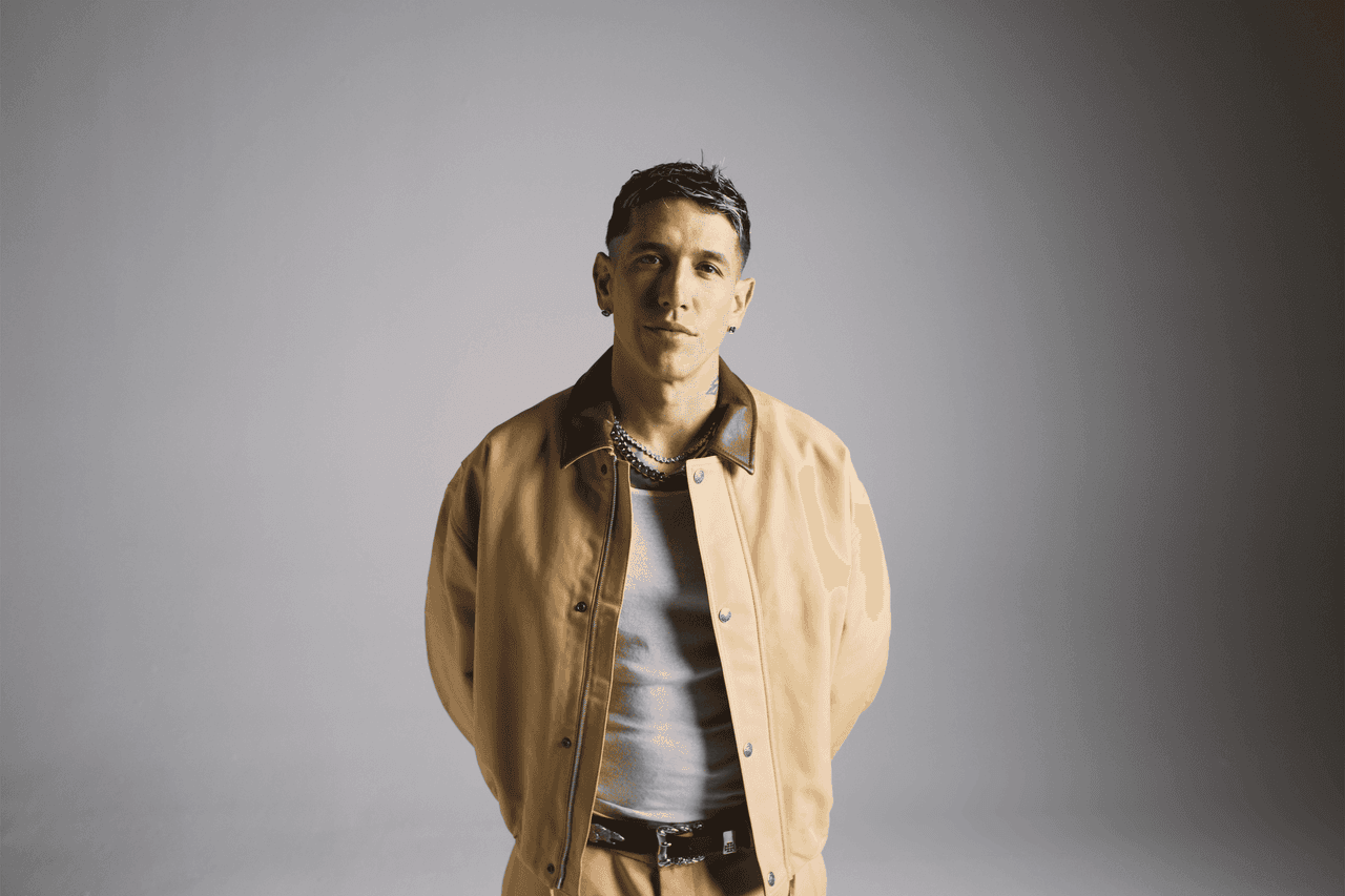 Lenny Tavárez con chaqueta mostaza, la mano en el pecho