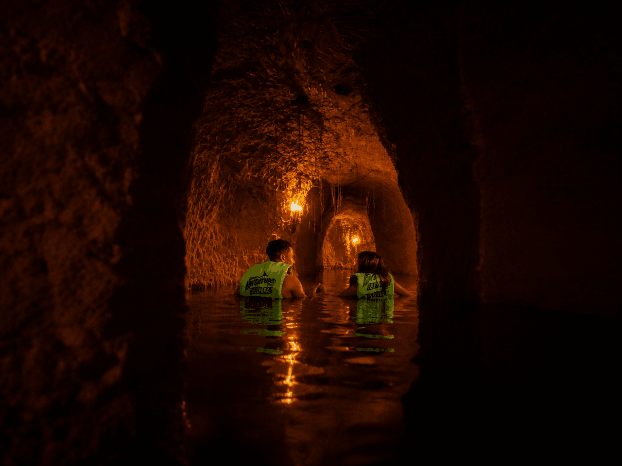 Dos visitantes recorren el río subterráneo bajo la luz de las antorchas