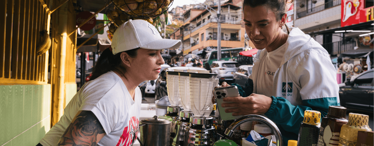 Dos mujeres consultan un teléfono móvil en un puesto de jugos en una calle