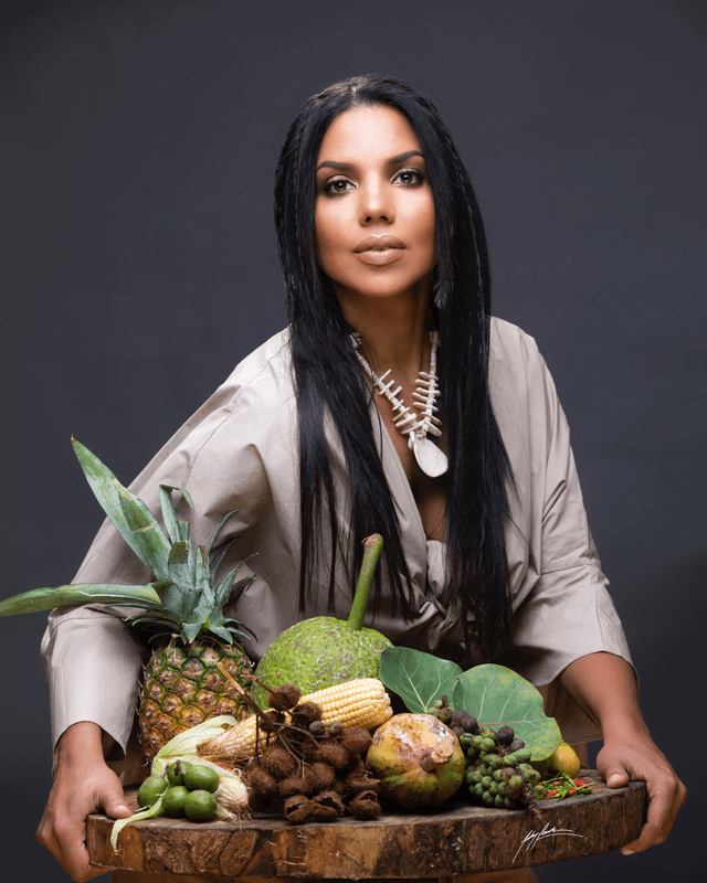 La chef dominicana Inés Páez Nin, Chef Tita, sostiene una bandeja de madera con piña, maíz, buen pan y otras frutas locales